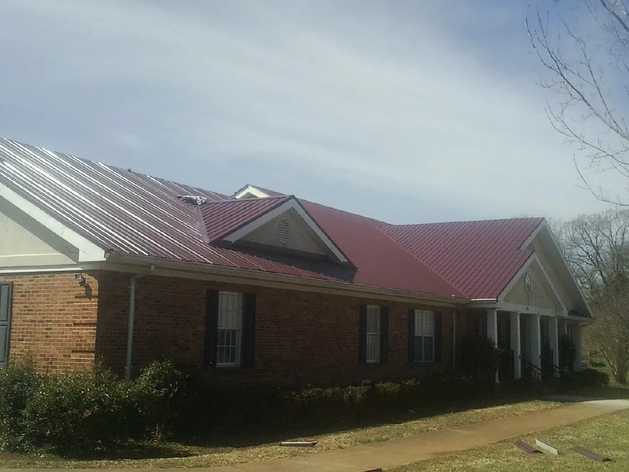 Red metal roof with gabled entries on a long brick building, from a Hail Damage Roof Repair job in McCammon