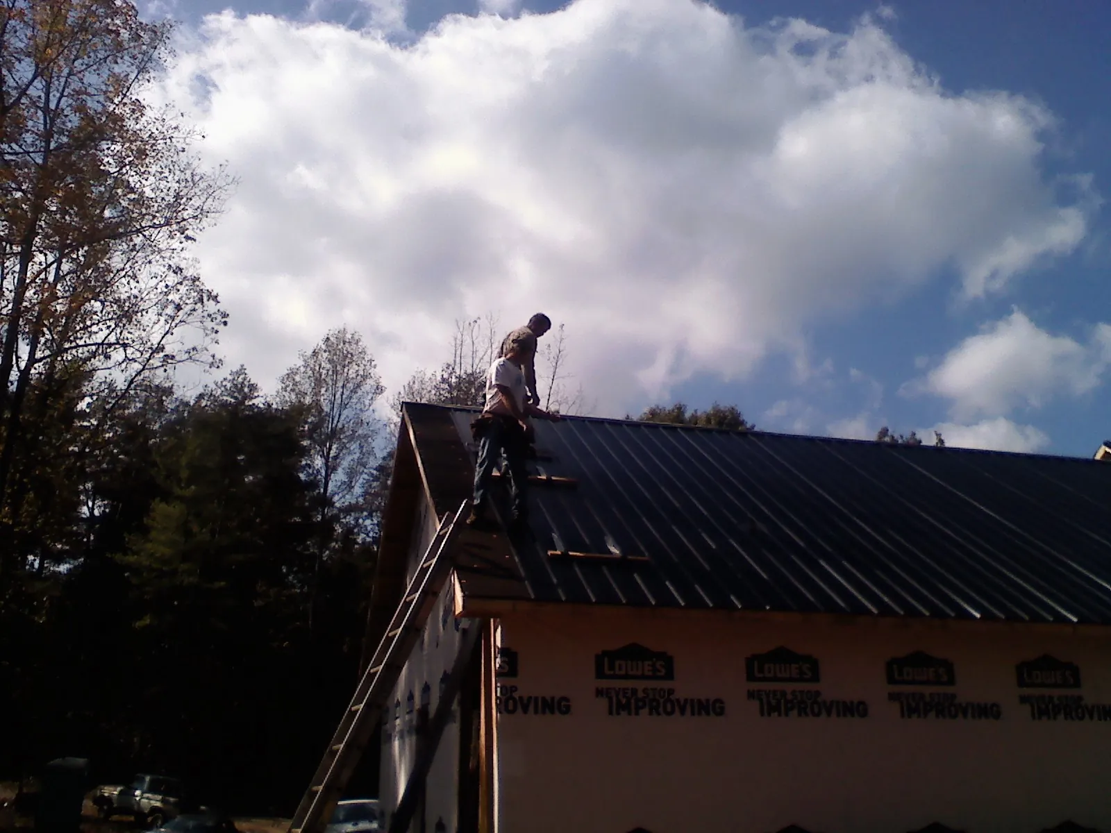 Roofer fastening dark metal panels high against a cloudy sky, from a Roof Inspection job in McCammon