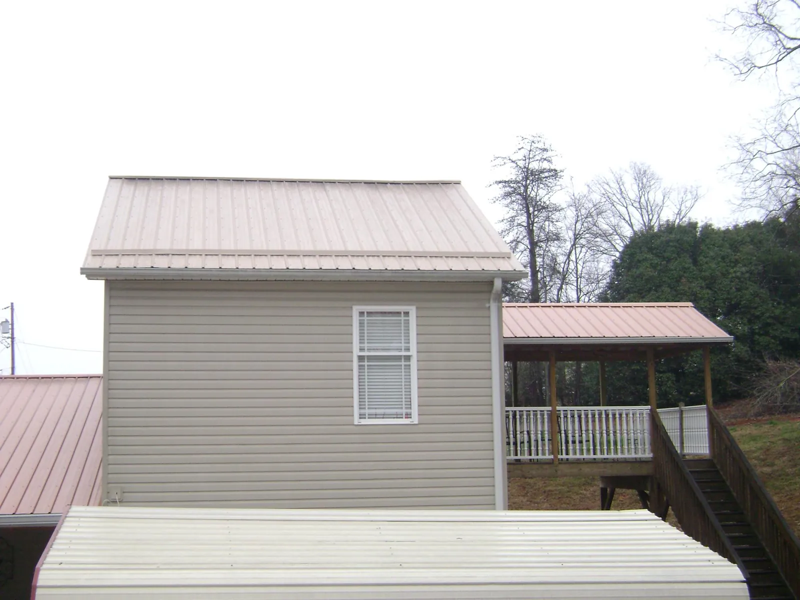 Tan metal roofs on a two story addition and attached porch, from a Roof Replacement job in McCammon